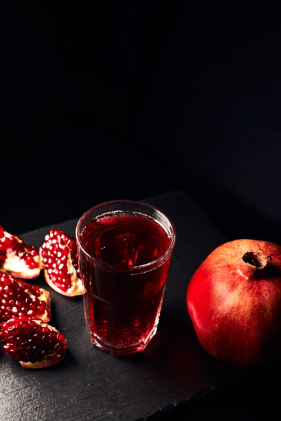 Pomegranate juice on a dark background. Pieces of pomegranate on a dark background. Summer drink. - Photo, Image