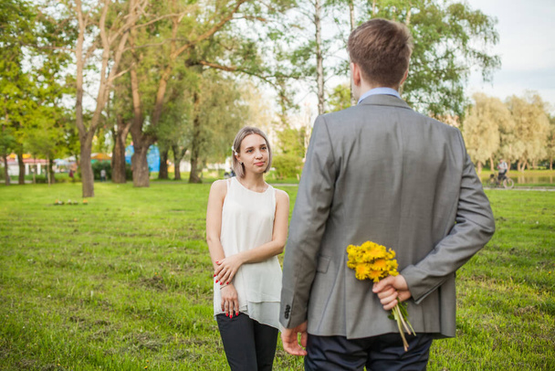 Young woman looking at man with flowers outdoors - Photo, image
