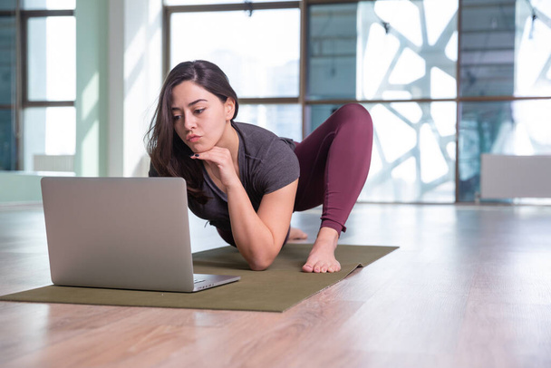 Photo d'une jeune femme pratiquant le yoga avec un ordinateur portable pendant une pandémie. Belle fille pratique le yoga en classe. Professeur de yoga studio. Fond flou
 - Photo, image