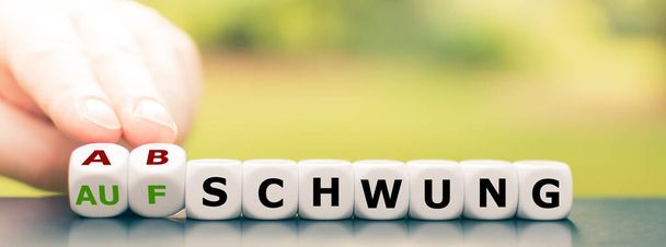 Symbol pro pokles ekonomiky. Ruka otočí kostky a změní německé slovo "Aufschwung" ("boom") na "Abschwung" ("downswing"). - Fotografie, Obrázek