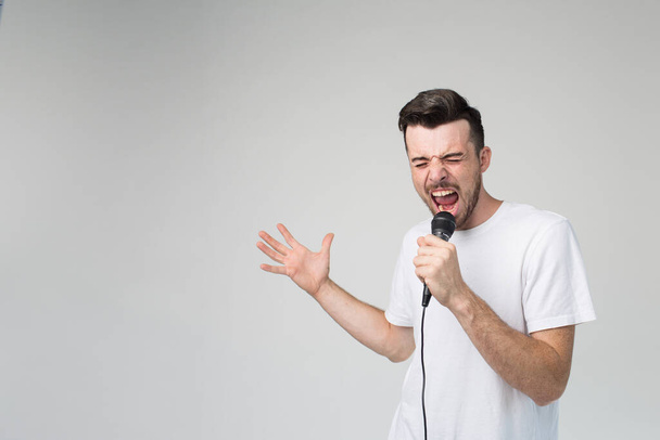 Young man isolated over background. Sing song alone in studio room. Hold microphone in hands. Karaoke time. Sing out loud and scream. - Fotografie, Obrázek