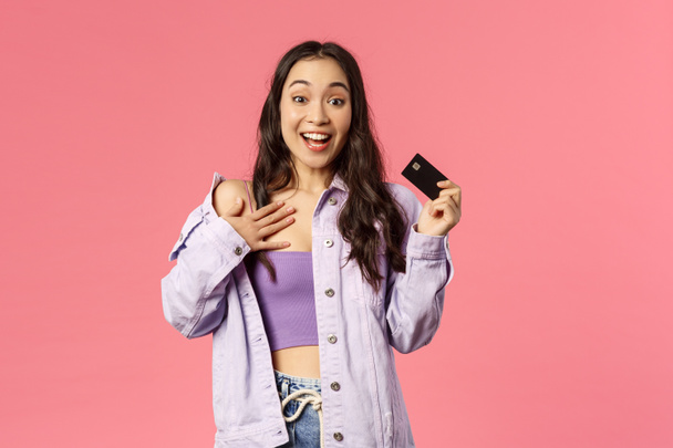 Porträt eines aufgeregten, begeisterten jungen Mädchens, das Kreditkarte in der Hand hält, keucht und die Brust berührt, als sei es überwältigt von der neuen Kleidersammlung im Online-Shop, bereit, Geld zu kaufen und zu verschwenden - Foto, Bild