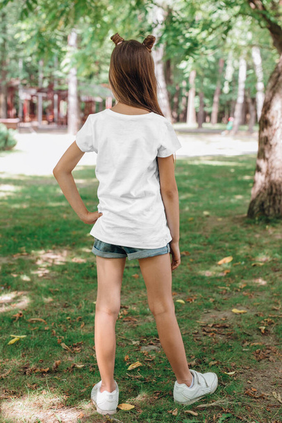 back views of little girl in blank t-shirt in park. Mockup for design - Fotografie, Obrázek