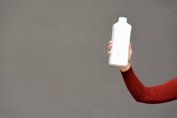 White detergent bottle in female hand on gray background. - Fotografie, Obrázek