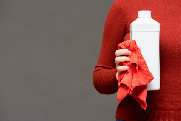 White detergent bottle and rag in female hand on gray background. - Foto, afbeelding