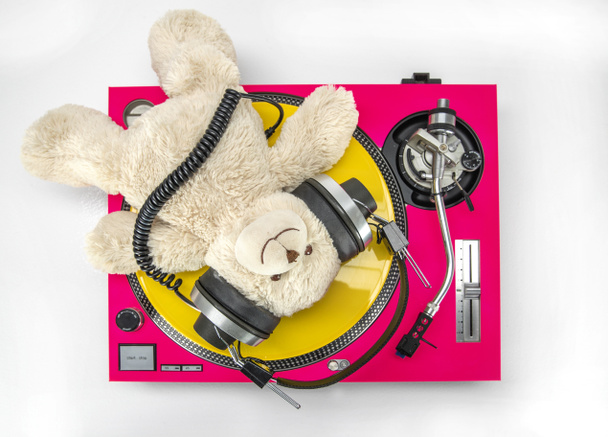 een coole DJ teddybeer liggend en ontspannend bovenop roze draaitafel met geel vinyl - Foto, afbeelding