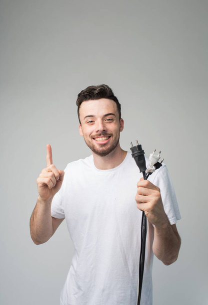 Young man isolated over background. Guy with socket and cord in hands pointing on it and smile on camera. Picture of young master ready to repair. Point up with pleasure. - Фото, зображення