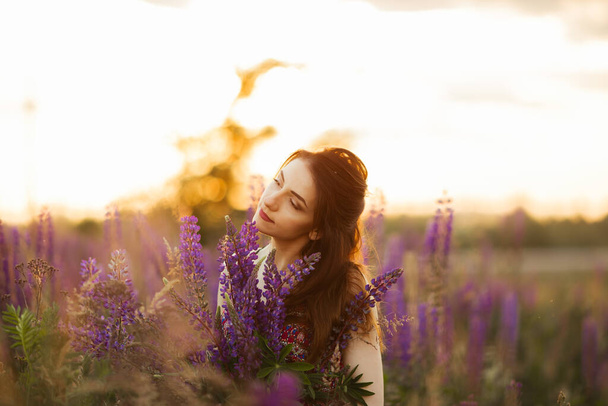 Young girl stand in field overlooking lavender field. Smiling carefree caucasian girl in dress enjoying the sunset. - Photo, image