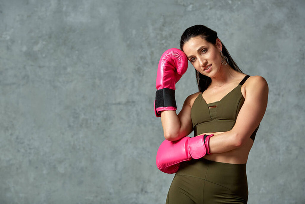 Hermosa chica atlética posando en guantes de boxeo rosa sobre un fondo gris. Copiar espacio. Concepto deporte, lucha, logro de metas
. - Foto, imagen