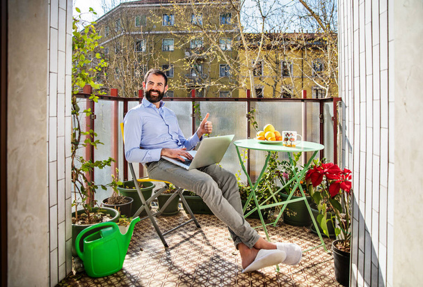Empresario en el trabajo inteligente usando el ordenador portátil sentado en el balcón en su casa
 - Foto, Imagen