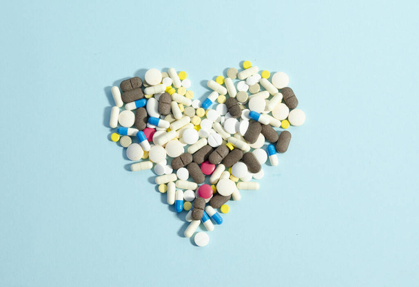 Pills laying in a heart shape on blue background. Different pills together. - Photo, Image