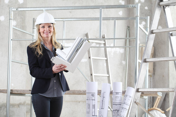 femme souriante architecte ou architecte d'intérieur de construction avec des fenêtres blanches profil coupant à l'intérieur d'un chantier de construction avec échelle et échafaudage en arrière-plan
 - Photo, image