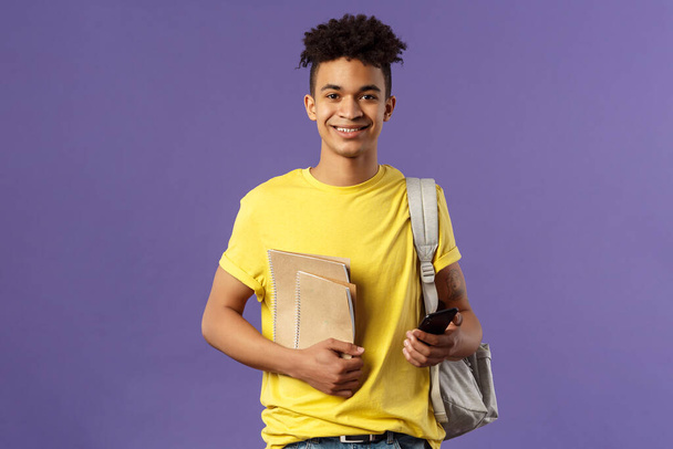 De vuelta a la escuela, concepto universitario. Retrato de un joven estudiante alegre con rastas, hipster yendo a su campus, llevar mochila y material de estudio, cuadernos, fondo púrpura
 - Foto, Imagen