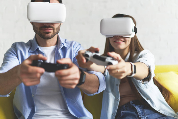 Closeup view of young smiling couple in VR glasses playing video game on the couch - Photo, Image