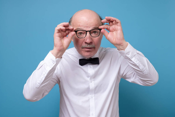 Amazed senior man looking at camera through glasses having some doubts over colored background - Fotoğraf, Görsel