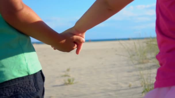 Κοντινό πλάνο μικρού αγοριού και κοριτσιού με ροζ φούστα που κρατιούνται χέρι-χέρι στην παραλία - Πλάνα, βίντεο