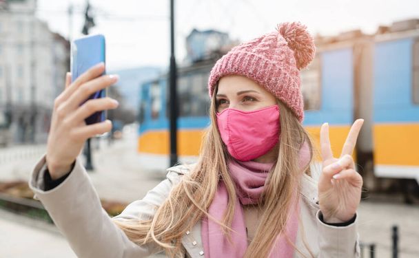 Frau macht Siegeszeichen und macht Selfie mit Handy mit Maske - Foto, Bild