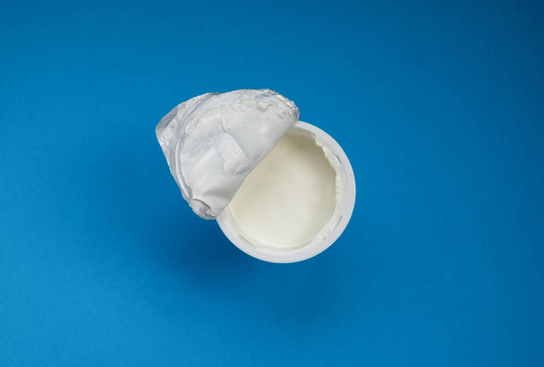 Otevřená sklenice s zakysanou smetanou nebo jogurtem s fóliovým víčkem. - Fotografie, Obrázek