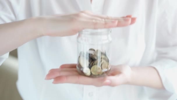 Closeup βίντεο αργή κίνηση της νεαρής γυναίκας ρίχνουν νομίσματα σε γυάλινο βάζο με εξοικονόμηση χρημάτων και ανακίνηση. Οικονομική κρίση - Πλάνα, βίντεο