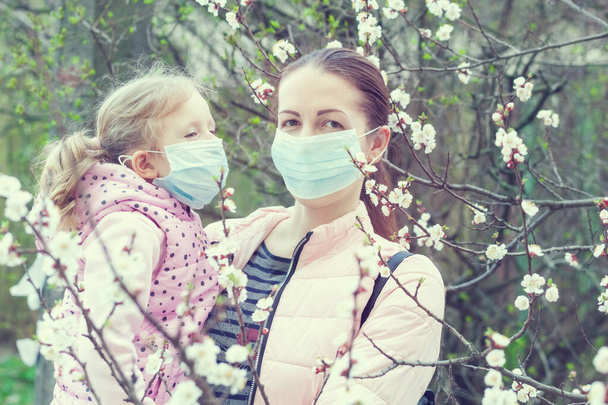 Portrait of a mom and daughter in masks on the street near a flowering tree. - Photo, Image