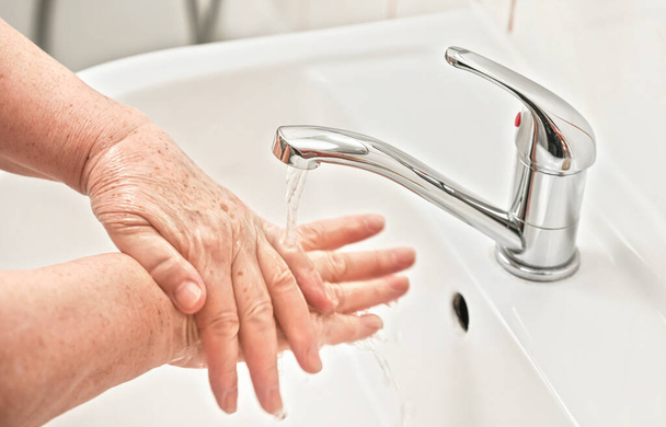 Starsza kobieta myje ręce mydłem pod kranem. Może być stosowany jako higieny ilustracji koncepcji podczas ncov coronavirus / covid 19 ognisko - Zdjęcie, obraz