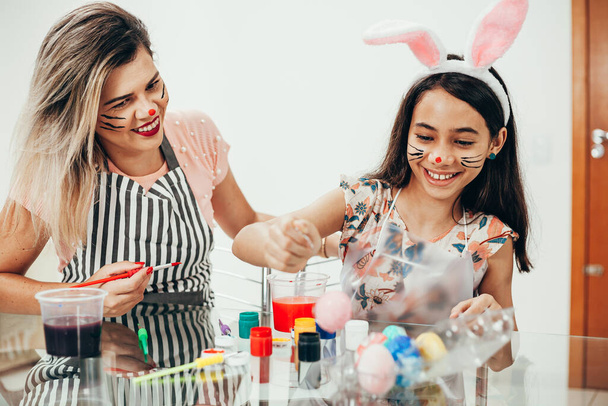 A mother and her daughter painting Easter eggs. Happy family preparing for Easter. Cute little girl wearing bunny ears on Easter day. Happy easter! - Valokuva, kuva