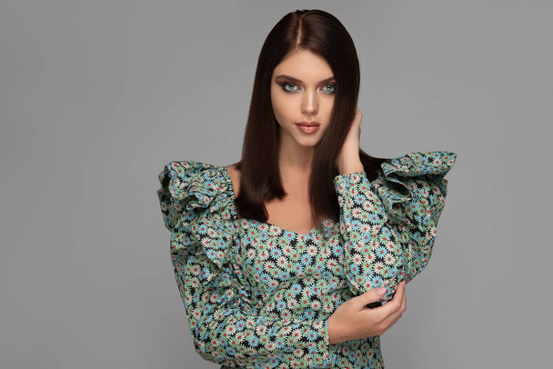 Fashion portrait of a beautiful young brunette with straight hair in a fashionable dress in a floral print and voluminous sleeves - Zdjęcie, obraz