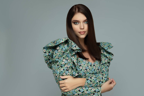 Fashion portrait of a beautiful young brunette with straight hair in a fashionable dress in a floral print and voluminous sleeves - Zdjęcie, obraz