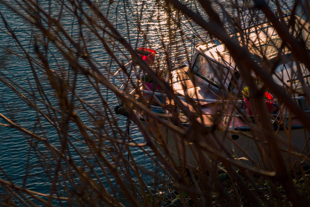 Jachta plovoucí na zvlněném povrchu moře, zatímco kotvící na břehu vidět mezi holými větvemi stromu na jaře - Fotografie, Obrázek