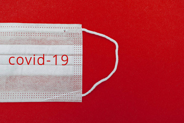 Medical disposable face mask on a red background with the inscription Kovid 19. World pandemic coronavirus. Stop the pandemic. Health and prevention of influenza and an infectious outbreak. Quarantine - Photo, Image