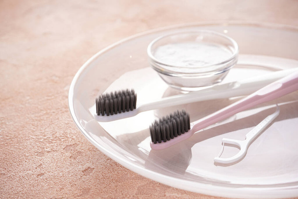 Zwei Zahnbürsten mit schwarzen Borsten, ein Zahnstocher und Zahnpasta auf beigem Hintergrund, Nahaufnahme. - Foto, Bild