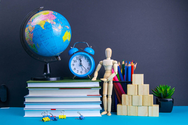 The globe and the clock stand on a stack of books, next to a glass of pencils and the pyramid is folded with wooden cubes and the figure of a wooden man. - Photo, Image