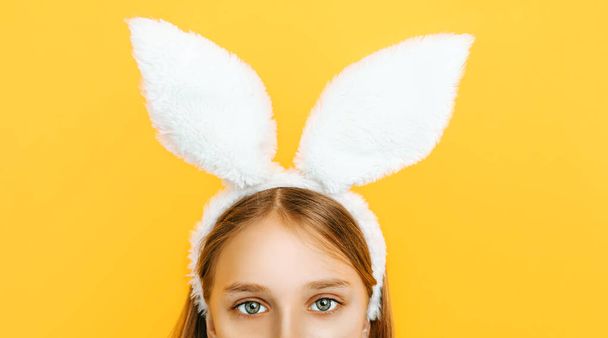 Happy little beautiful girl on her head with rabbit ears, posing on a yellow background. Symbol of Easter and spring. - Φωτογραφία, εικόνα