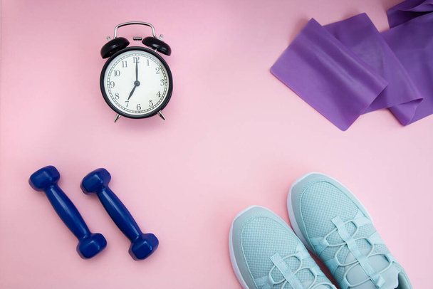 sneakers, dumbbells, training tape and a black alarm clock are on a pink background. Sports flat lay. Time for sports at home. Quarantined Sports. Healthy body. - Photo, Image