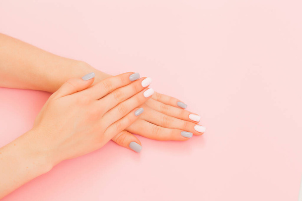 Closeup of hands of a young woman with manicure on nails against pink background - Photo, image