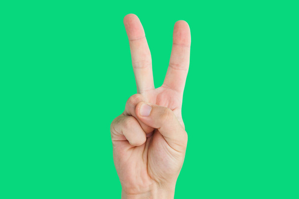 Мужская рука показывает знак мира с пальцами на зеленом фоне. - Фото, изображение