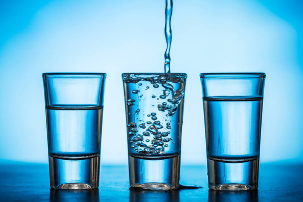 water being poured into small glasses on blue background - Photo, Image