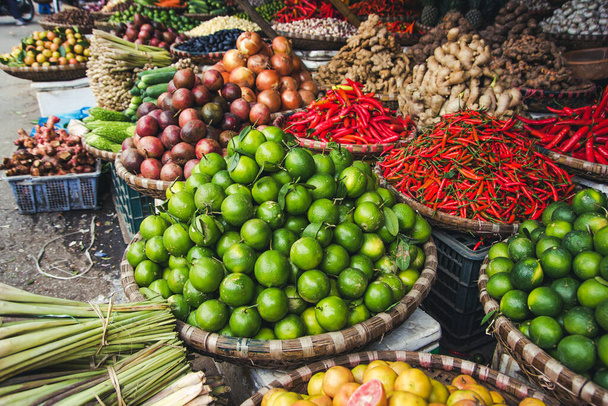 Green limes fruits stacked. Red chili peppers pile in wicker basket. Vegetable market in Vietnam. Vibrant color spicy food ingredient. Empty copy space grocery shopping background. - Photo, Image