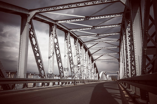金属製の橋の背景。道路橋の建設。空のアスファルトの道路。川を渡る嵐の天気の長い橋。ポーランドのTykocin村. - 写真・画像