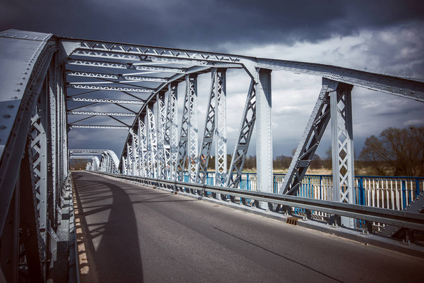 Metallbrücke Hintergrund. Brückenbau. Leere Asphaltstraße. Stürmisches Wetter lange Brücke über den Fluss. Tykocin-Dorf in Polen. - Foto, Bild