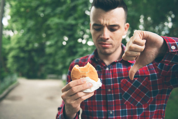 Man opening a hamburger. Man is eating in the park - Фото, зображення
