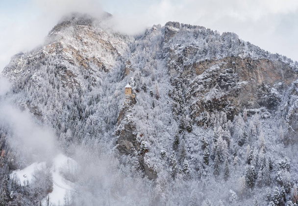 Vista aérea da montanha com torre de contorno, floresta sob nevoeiro, encostas com neve coberta na Suíça, atmosfera nublada, belas condições
 - Foto, Imagem