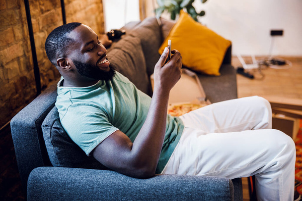 Gladsome man with smartphone on the sofa stock photo - Foto, afbeelding