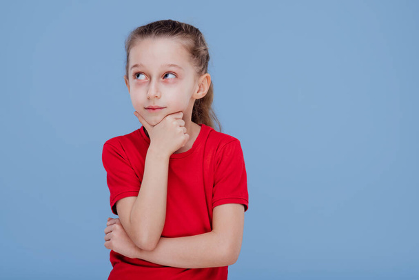 thinking little girl in red t shirt touching chin and looking away - Fotografie, Obrázek