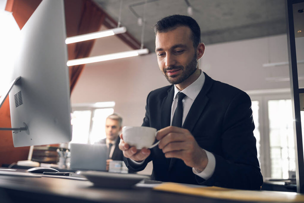 Caucasian attractive man drinking coffee at workplace in office - Valokuva, kuva