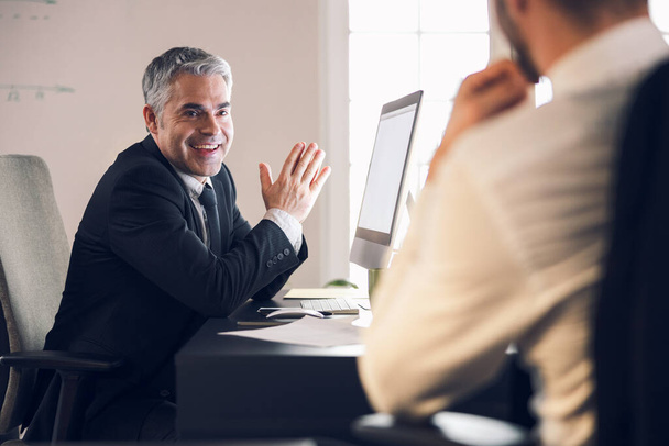 Smiling mature man talking to his colleague indoors - Фото, изображение