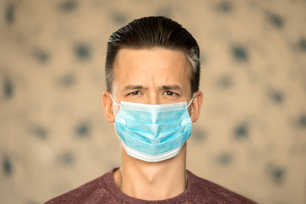 Θέμα κορωνοϊού και ασφάλειας. Ένας νεαρός με μπλε μάσκα από ιό φαίνεται απασχολημένος.. - Φωτογραφία, εικόνα