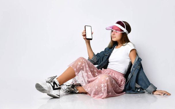 Smiling woman is pointing on smartphone standing on white background. - Φωτογραφία, εικόνα