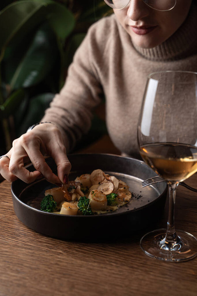 Young woman is eating roasted scallops with a glass of white wine - Photo, Image
