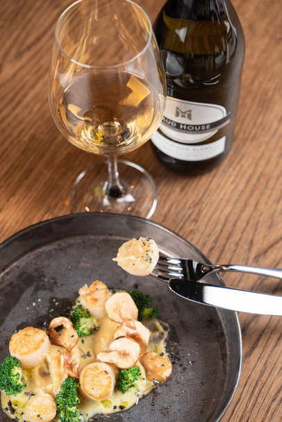 Close up of roasted scallop pinned on a fork with a glass on white wine - Fotoğraf, Görsel